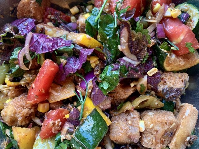 Close-up on a mess of food, with croutons, tomato, zucchini, and purple shiso visible