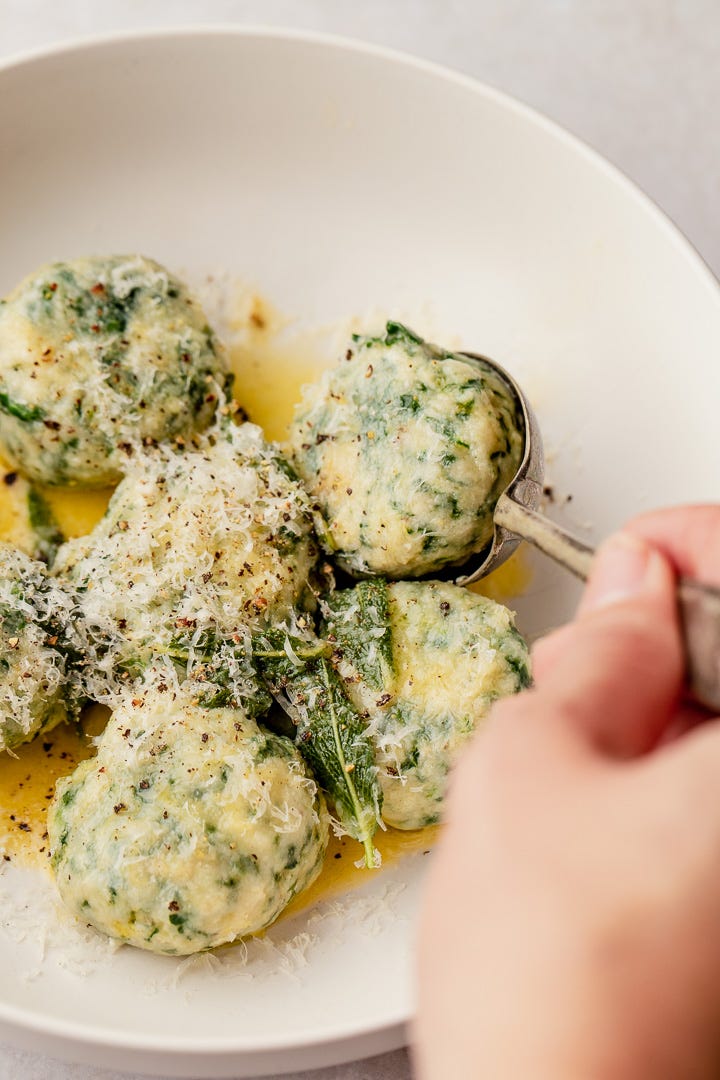 A white bowl with spinach and ricotta gnudi and a spoon lifting one of the dumplings.