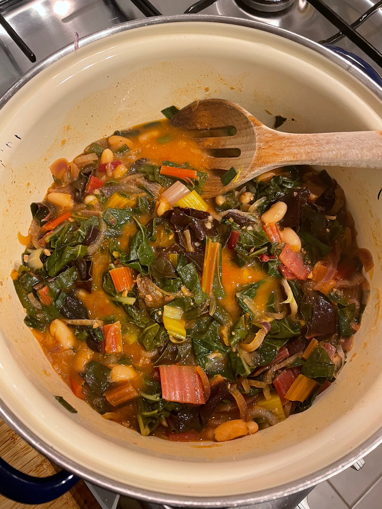 Rainbow chard, tinned beans, and red onion in a stew mixture on the stove.