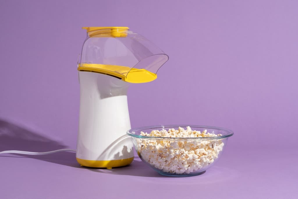 The air popper Presto PopLite next to a clear bowl full of popcorn