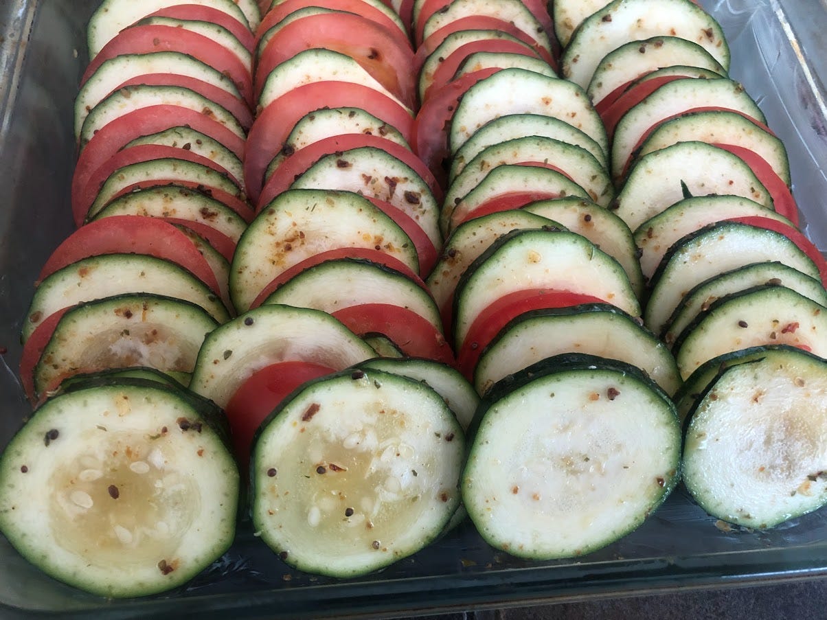 a square casserole dish with rows of zucchini and tomato slices