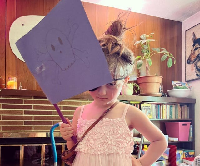My niece, dressed as a pirate — which for her meant a frilling pink dress, an eye patch, a spy glass, and a Jolly Roger flag that I drew for her. 