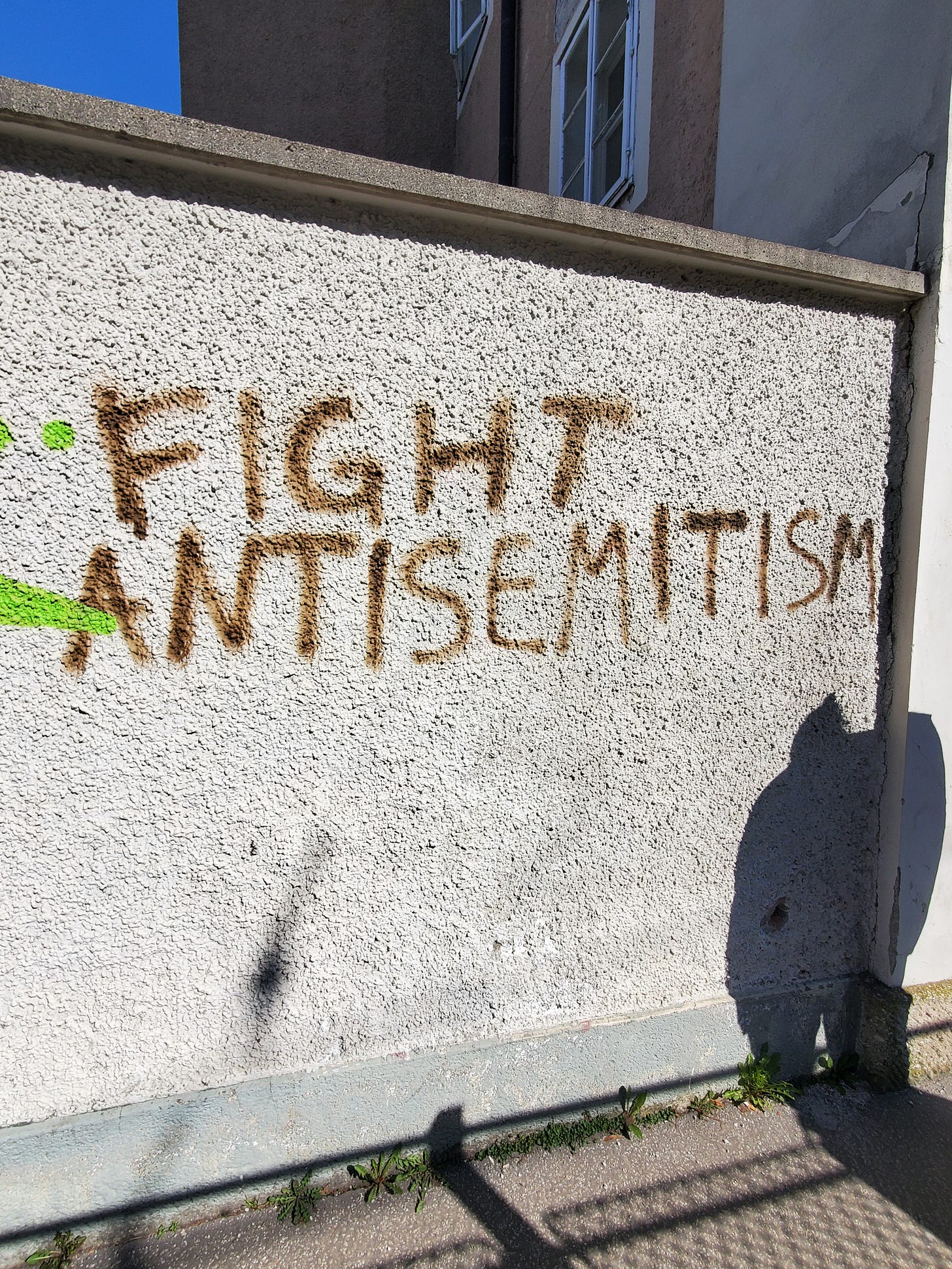 "Fight Antisemitism" in brown spray paint on a gray wall.