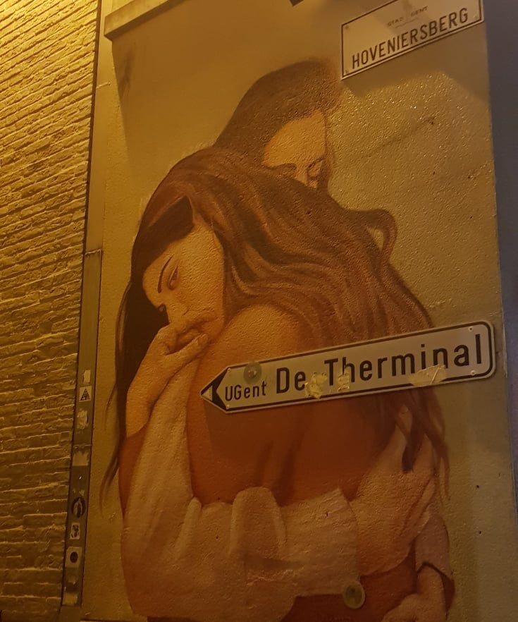 Street art mural of two women embracing. Photo is taken at night and on the street there is a sign that says 'UGent De Therminal'