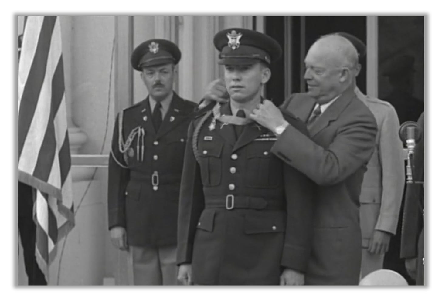 Dwight Eisenhower fastens a Medal of Honor around James Stone's neck. An American flag  is visible to the left.