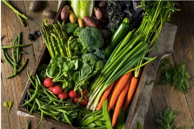 wooden table showing asparagus, broccoli, radishes, leeks, beans, peas, carrots and other raw vegetables