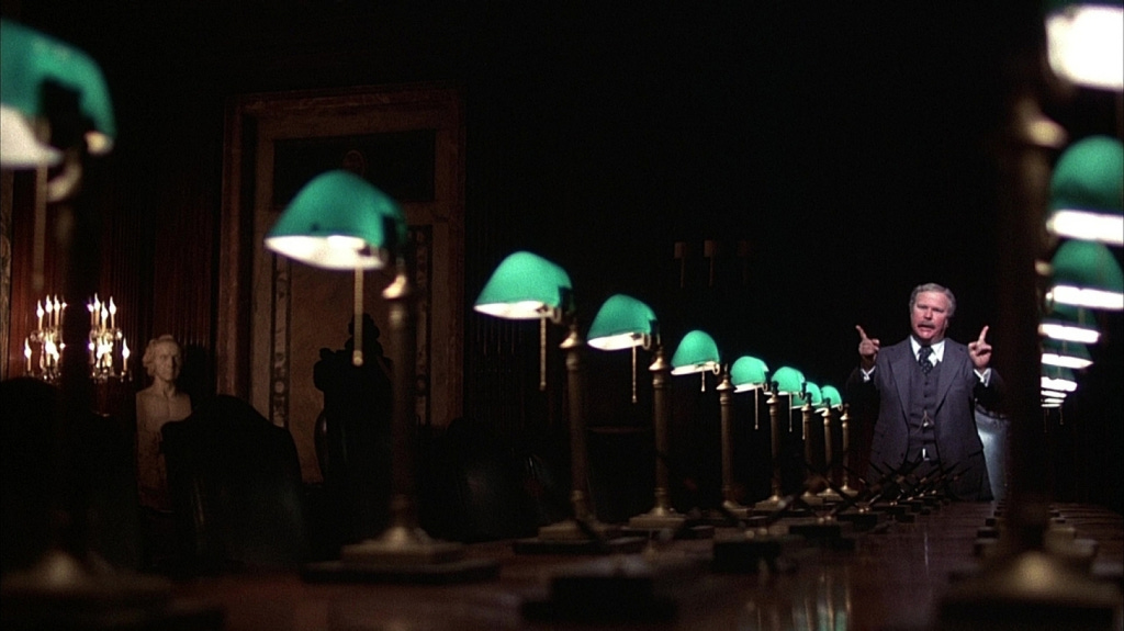 Arthur Jensen confronts Howard Beale in his darkened office, lit by green desk lamps, highlighting Jensen's authority.