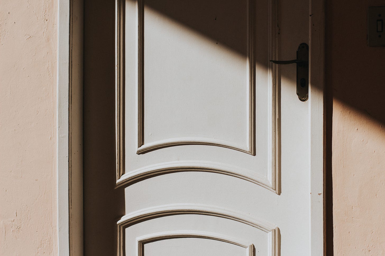 picture of a white door with curved paneling on a beige wall and half in shadow