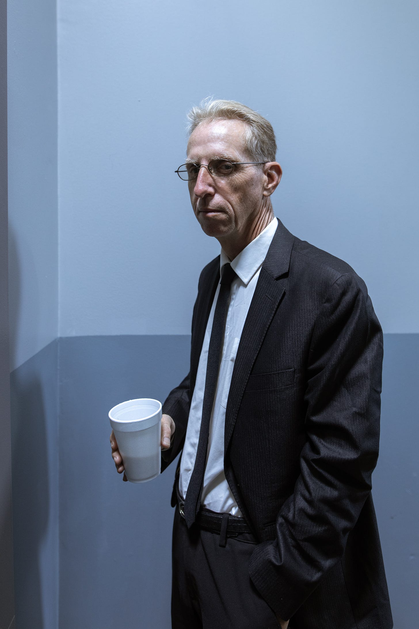 A middle aged man in a suit with a styrofoam cup of coffee. He looks like a cop.