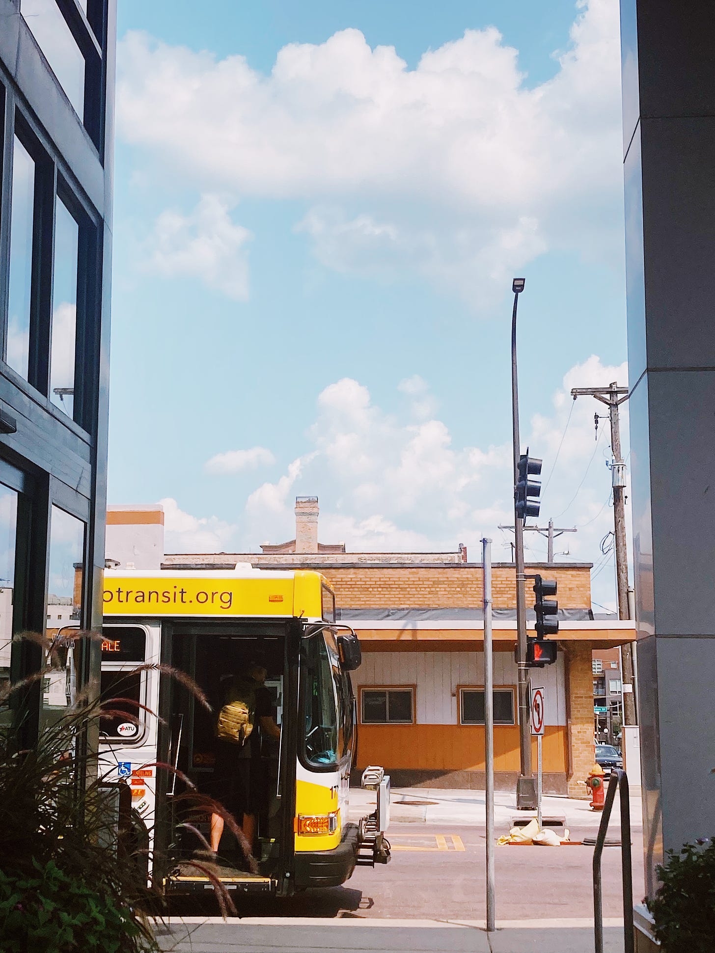 a passenger climbs onto a metro transit bus in front of a brick building and blue sky with white clouds