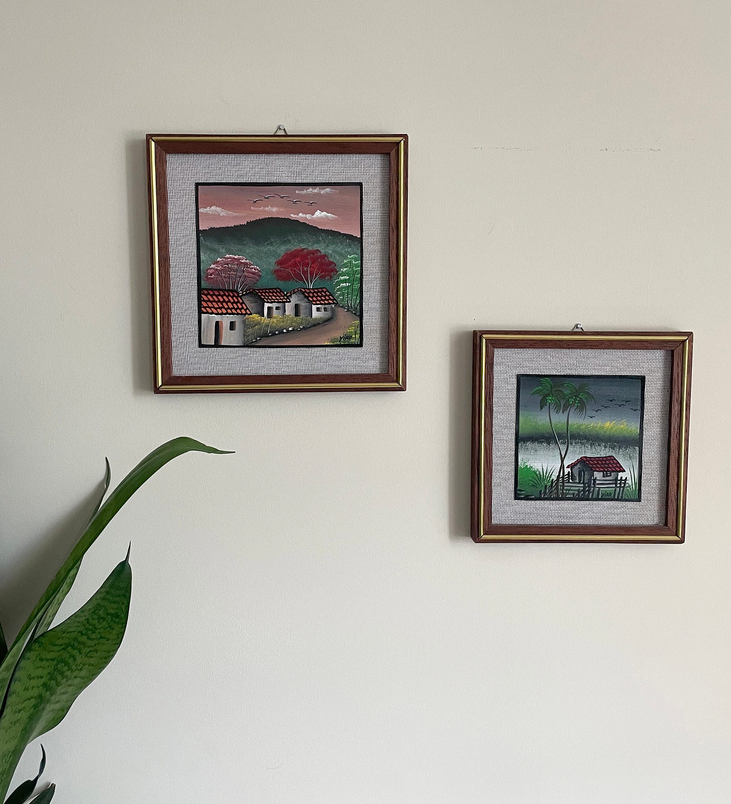 Two paintings depicting the countryside in El Salvador (houses, water, mountains).