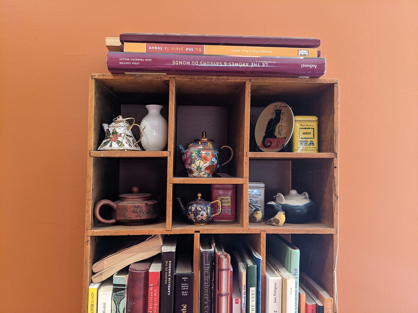 Wooden bookshelf with compartments for tea and shelves for books against orange wall. 