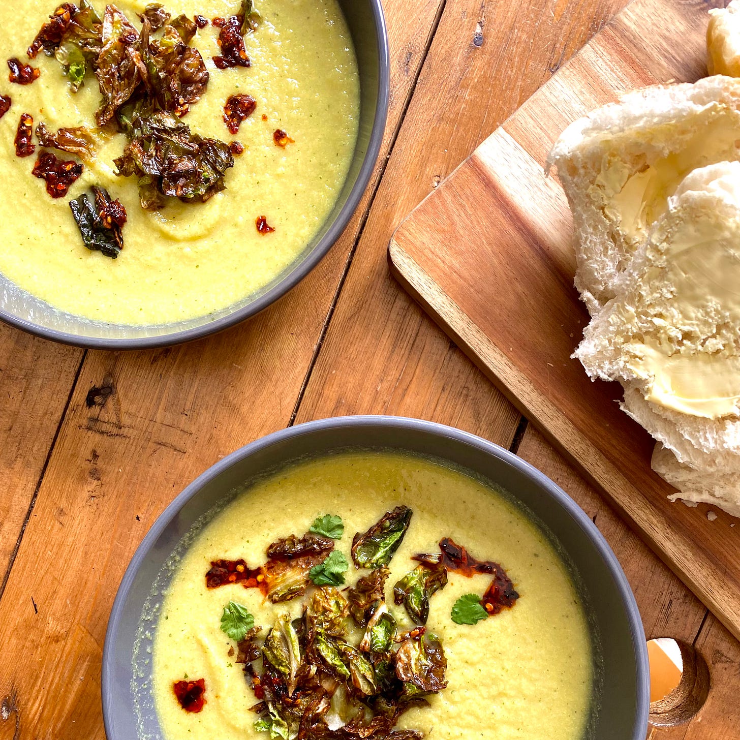 two bowls of cauliflower soup with a bread board and bread to the side