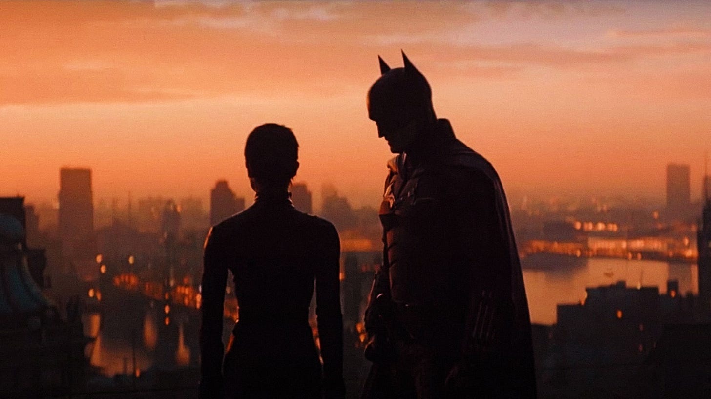 Batman and Catwoman over a sunset painted skyline of Gotham City.