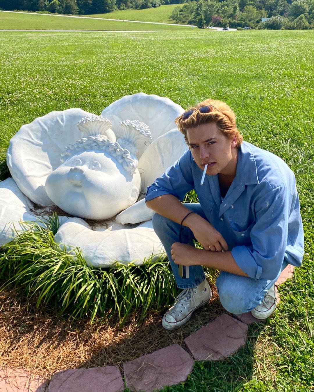 Cole Sprouse, dressed in all denim, kneels beside a stone statue of a Cabbage Patch Kid mid-birth, cigarette perched on the edge of his lips. Cole Sprouse, dressed in all denim, kneels beside a stone statue of a Cabbage Patch Kid mid-birth, cigarette perched on the edge of his lips.
