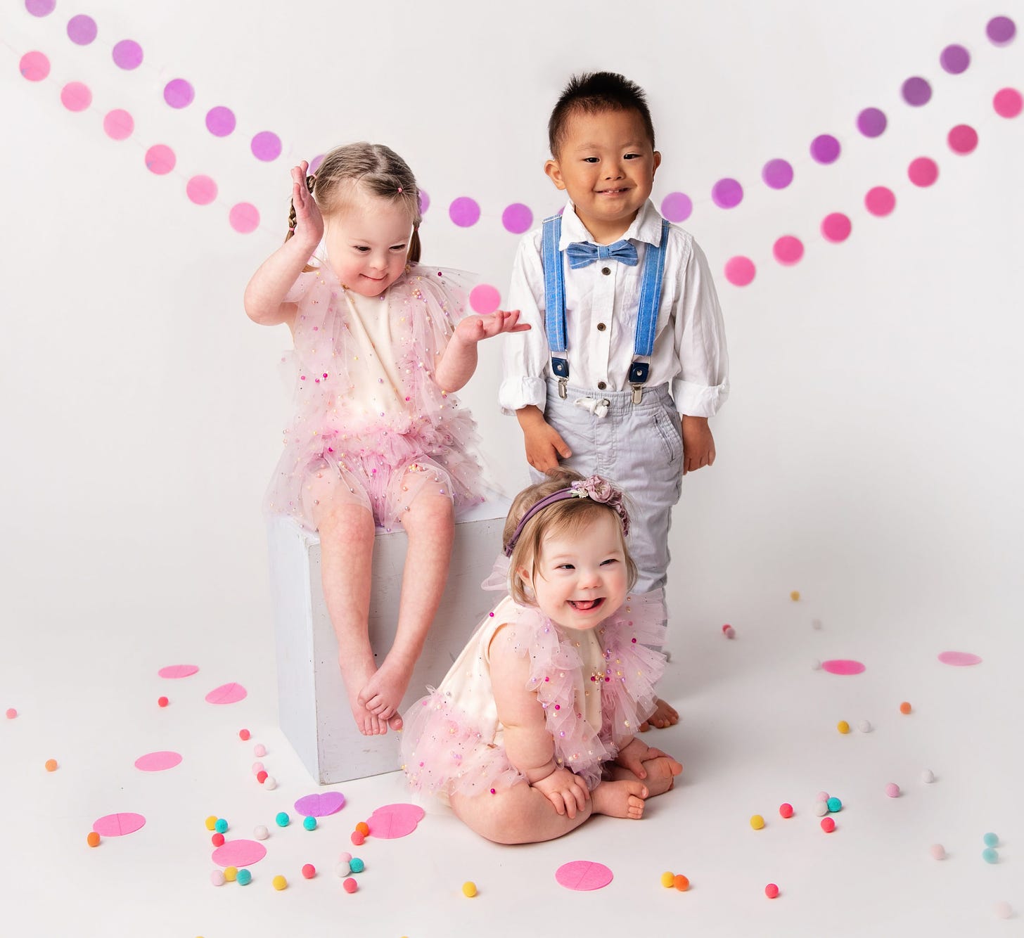 three small children smiling with white background and colorful dots .