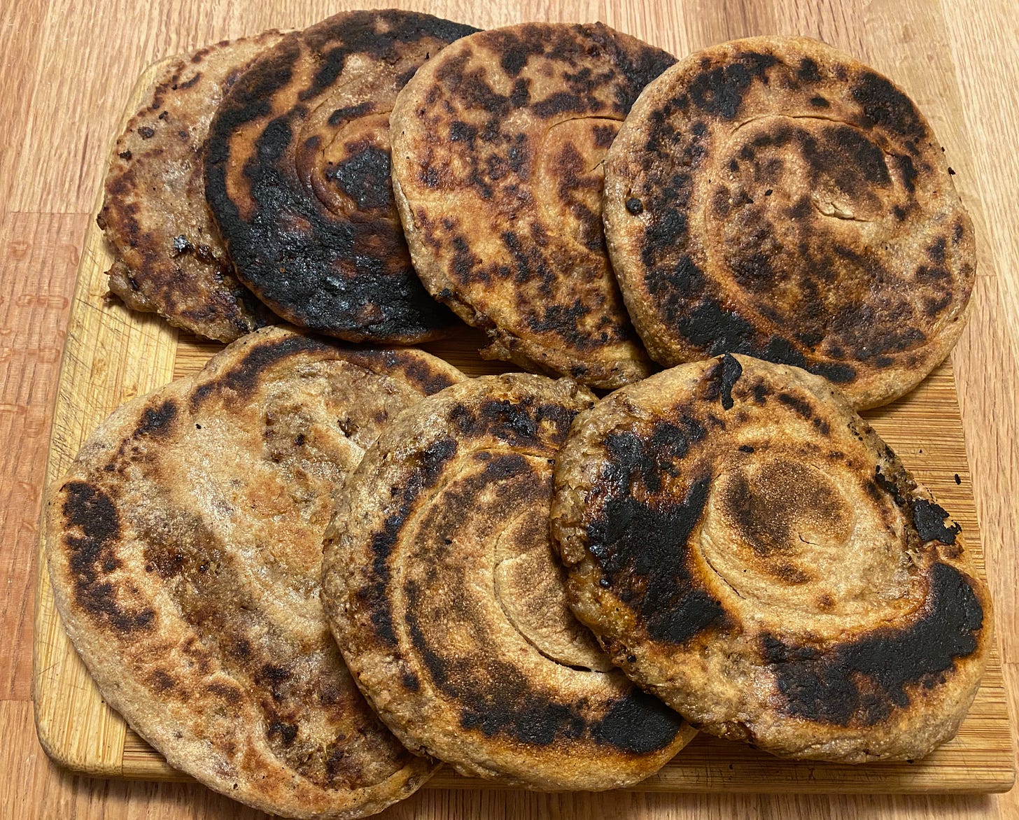 Eight round, charred flatbreads sit in two rows on a cutting board.