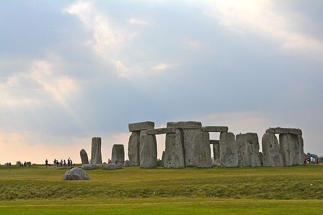 Image shows the standing stones of Stonehenge in front of bright sky with clouds, seemingly at dusk.