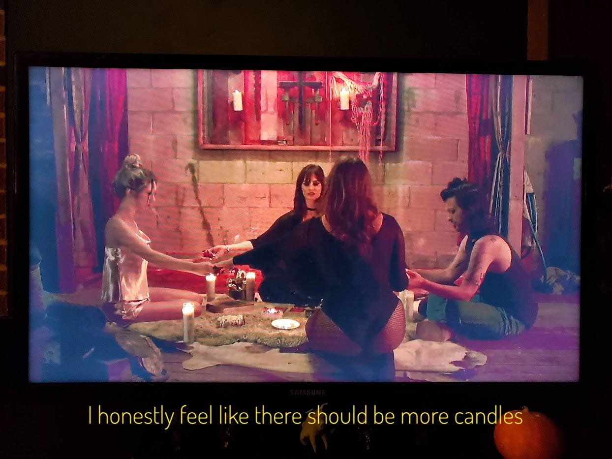 Grace and three goths joining hands sitting on an animal skin rug with lots of candles but not enough candles