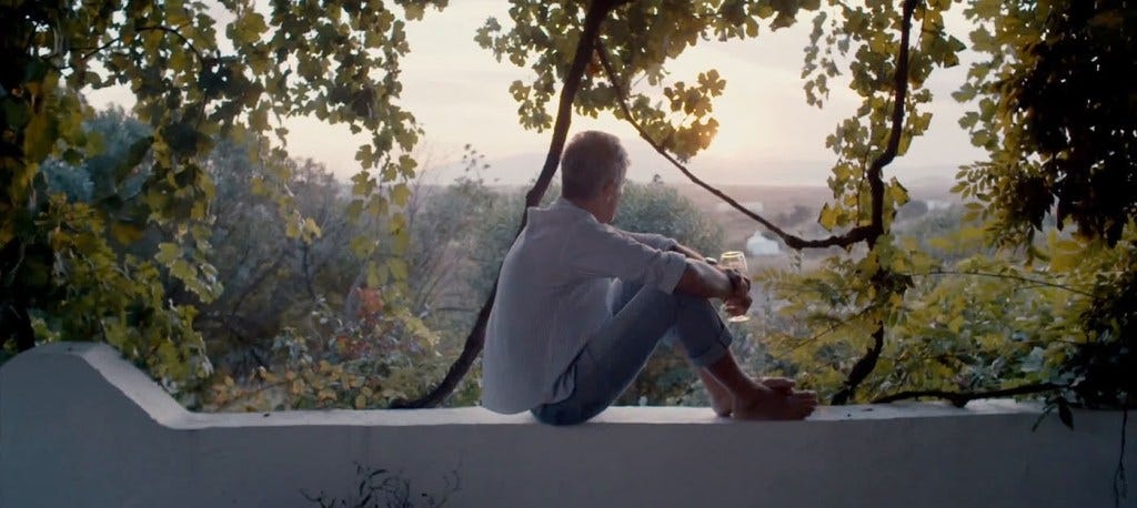 A still from Roadrunner. Anthony Bourdain sits alone on a ledge, surrounded by trees.