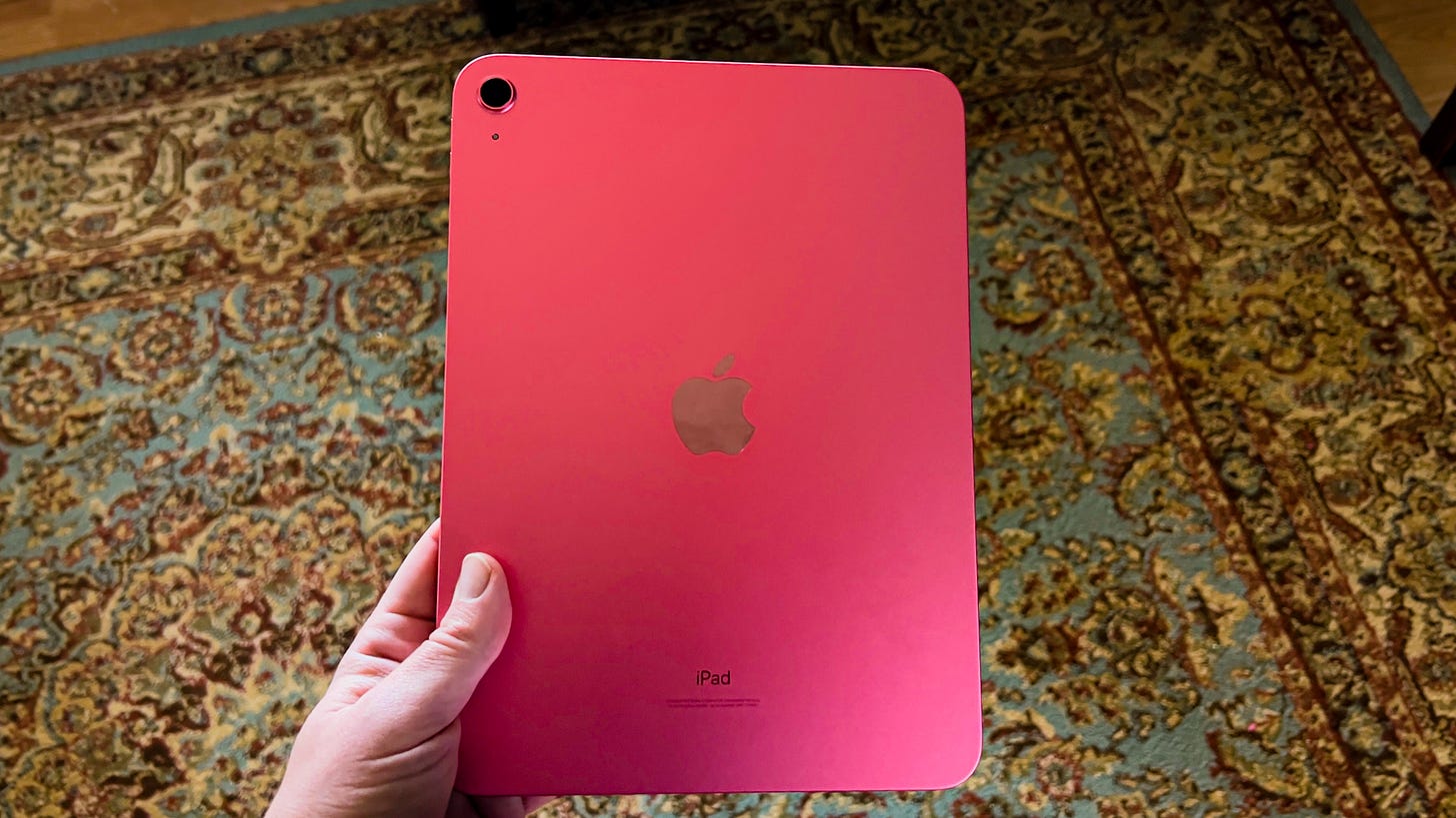 A pink 2022 iPad held over a patterned rug