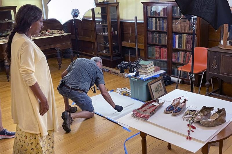 Leola One Feather, left, of the Oglala Sioux Tribe in South Dakota, observes as John Willis photographs Native American artifacts on July 19, 2022, at the Founders Museum in Barre, Massachusetts. The private museum, which is housed in the town library, is working to repatriate as many as 200 items believed to have been taken from Native Americans massacred by U.S. soldiers at Wounded Knee Creek in 1890. Willis is photographing the items for documentation, ahead of their expected return to the tribe. (AP Photo/Philip Marcelo)