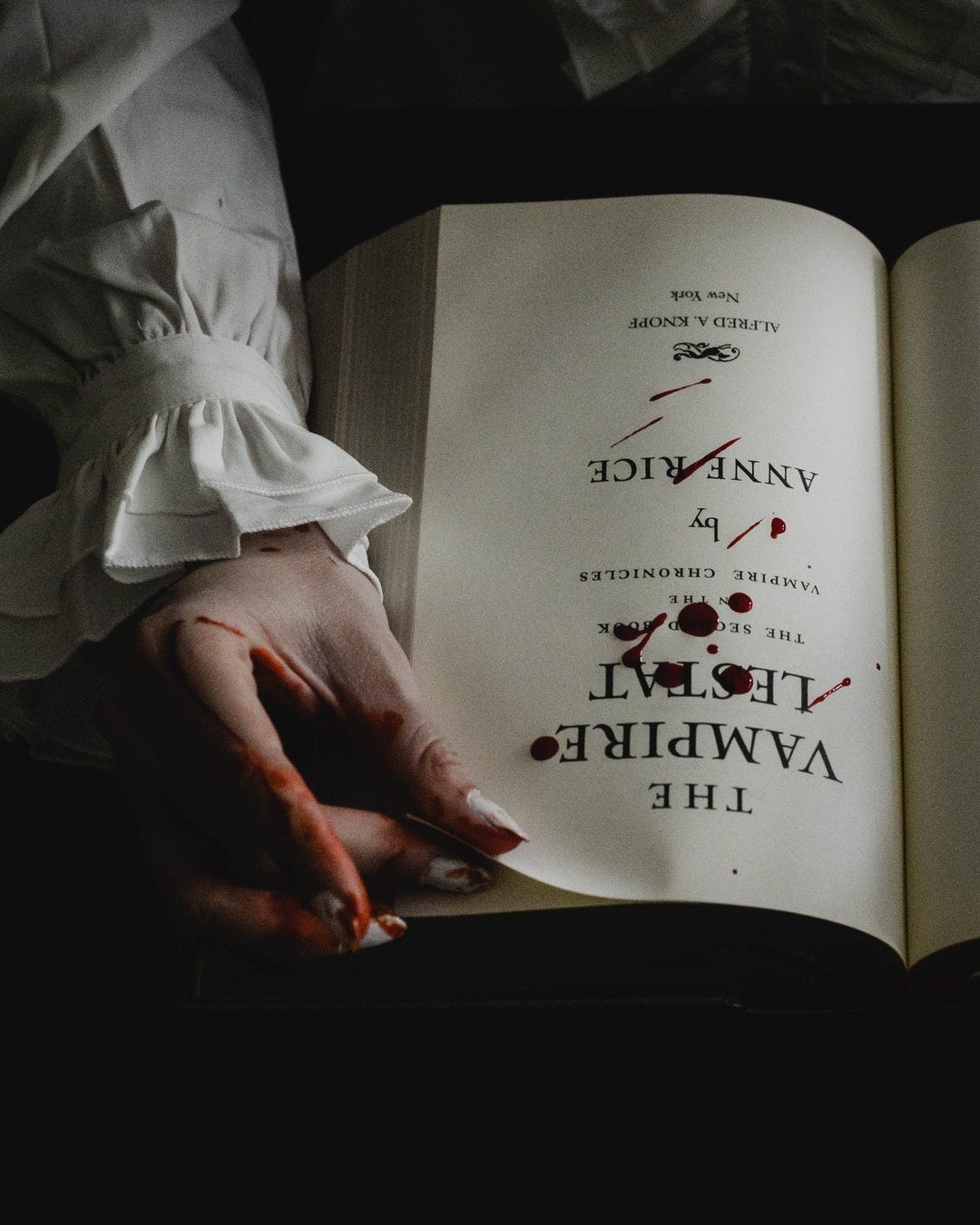 the vampire lestat book by anne rice opened with blood drops and streaks on the page, a hand stained in blood at the corner of the page