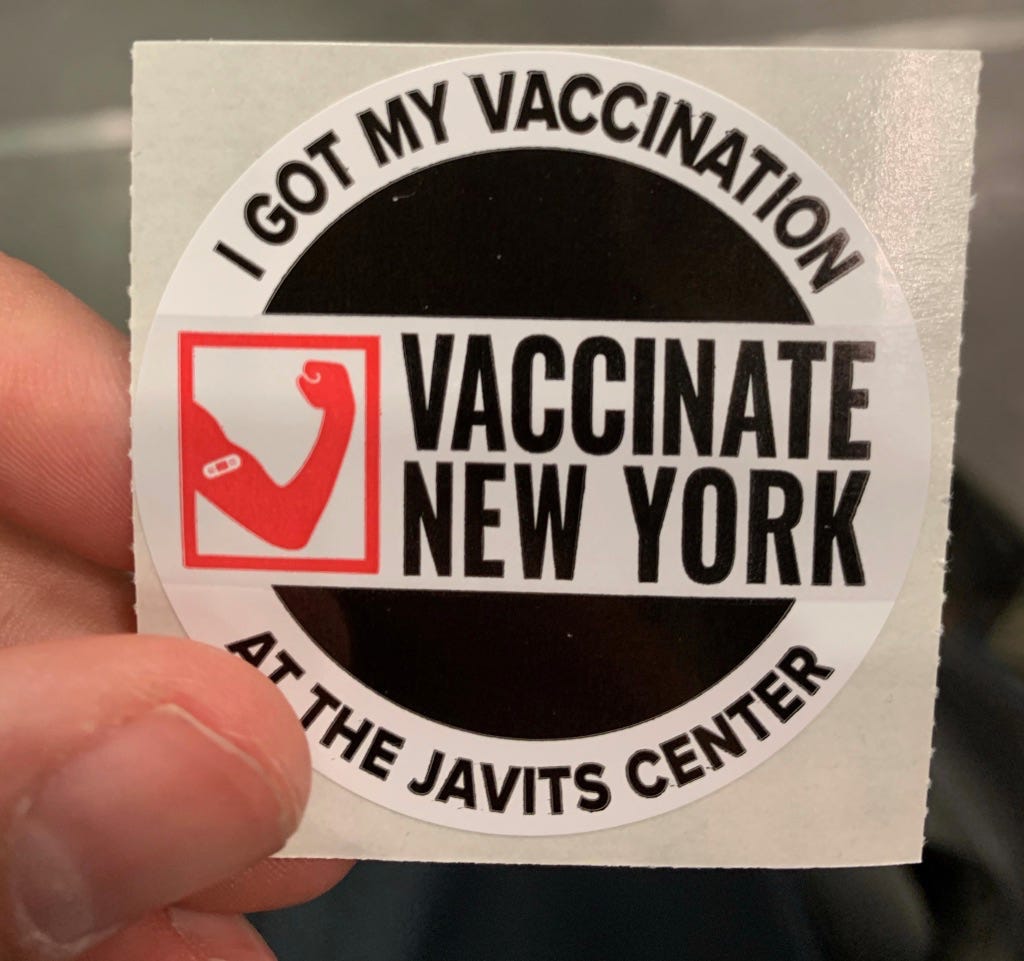 Image is a circular sticker with text circumscribing the circle, reading “I got my vaccination at the Javits Center. Inside the circle, there is an illustration of an arm with a band-aid on it, in red, and in black, the words “Vaccinate New York.”
