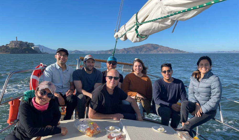 7 people, including Kevin sitting on a sail boat smiling.