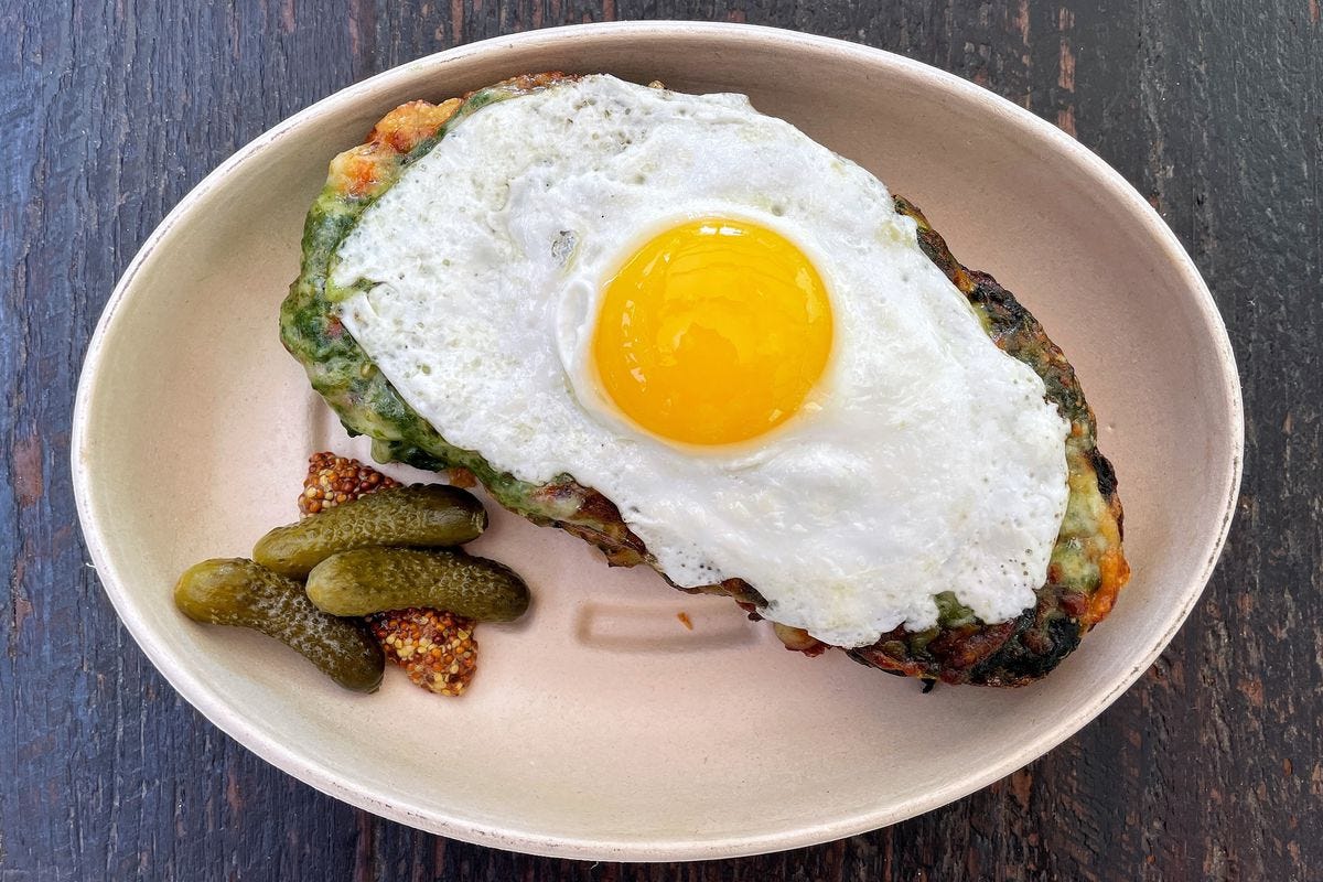 An overhead shot of Dirt Candy’s spinach croque monsieur, a sandwich topped with a fried egg, in a takeout container.