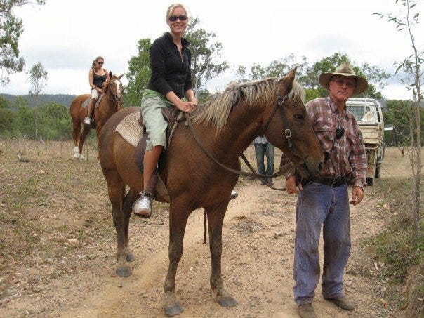 A young woman sits on a horse led by an older man on a farm in Australia.