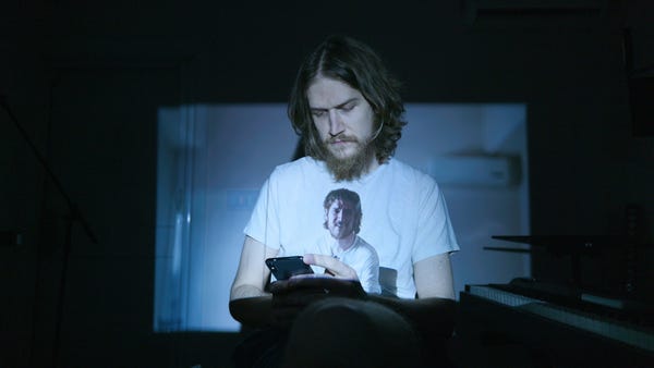 Bo Burnham usando o celular usando uma camiseta com a imagem de Bo Burnham