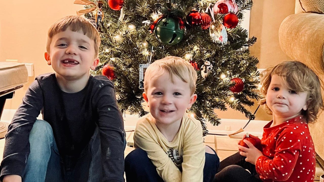 Three children sitting in front of a Christmas tree.