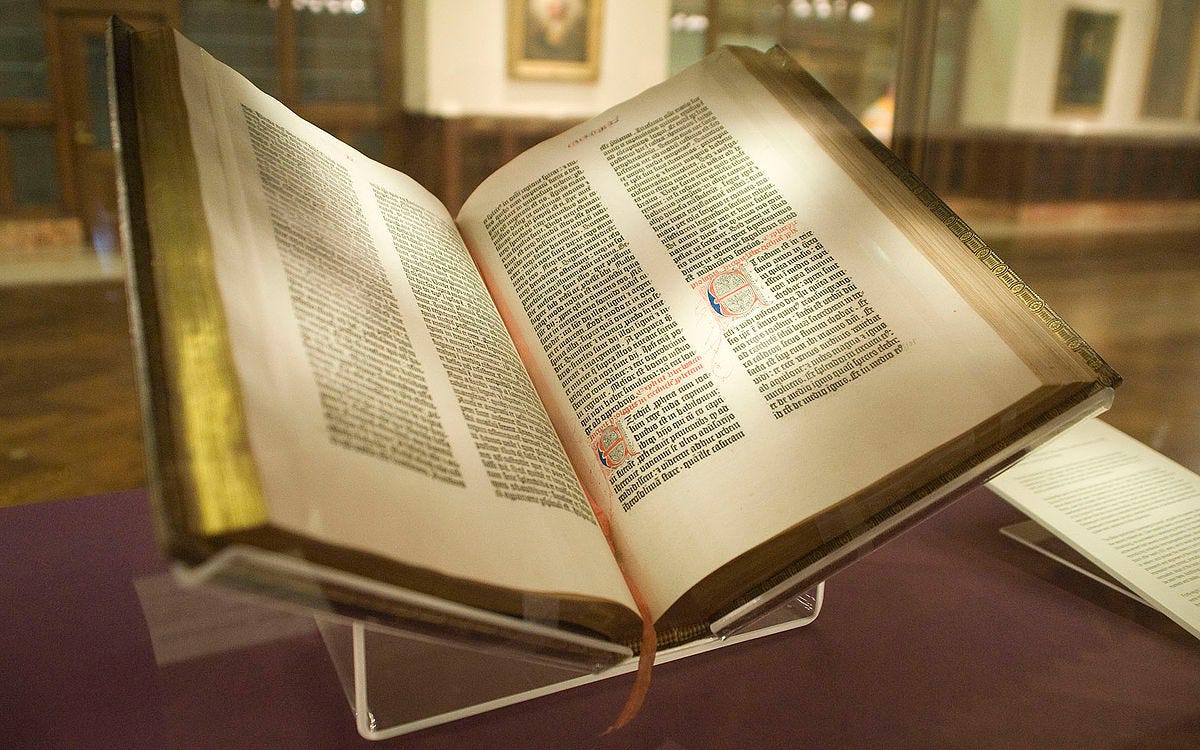 A Bible with gold-rimmed pages is set open on a book stand on a maroon table. Looks like English King James -- blocky intense letters et al. i think this is from a museum or something. looks real cool. can't read what it's turned to, but it's the middle of the bible or so