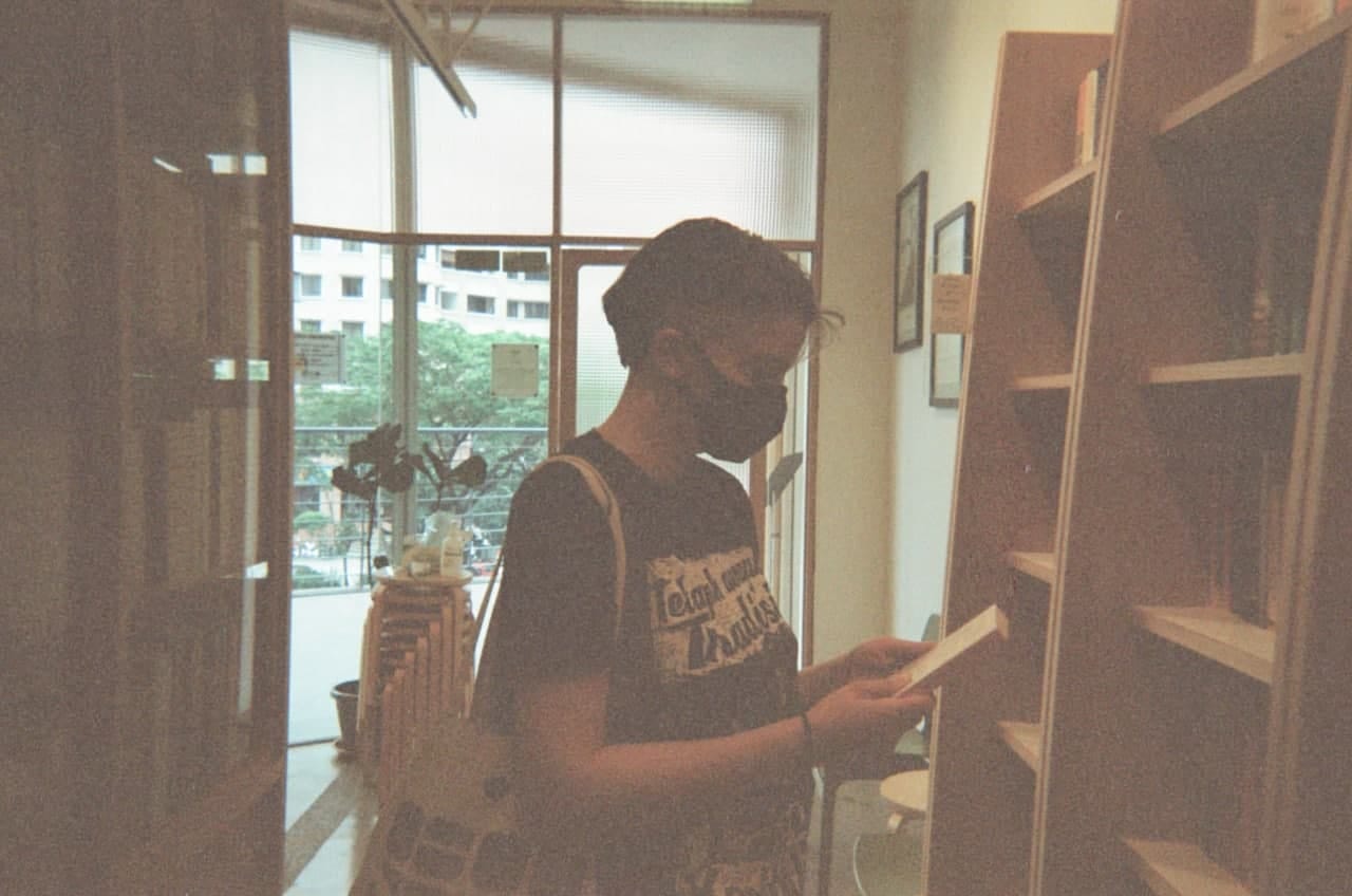 Nine, wearing a black face mask, looks at a book in a bookshop