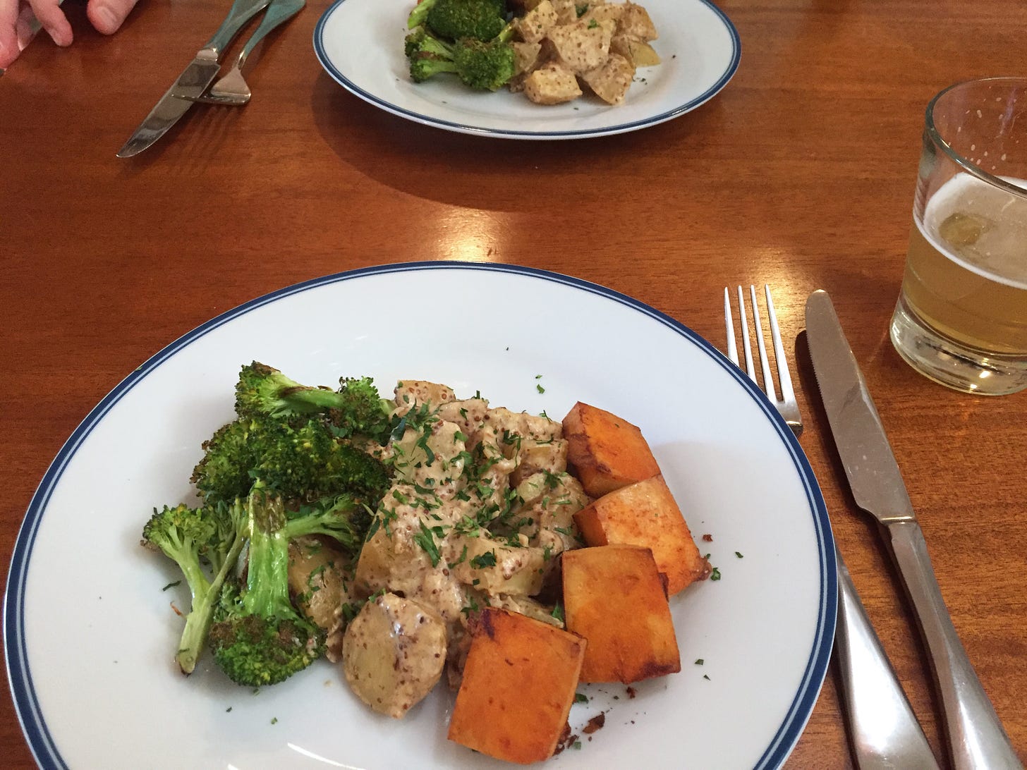 A plate of potato salad in grainy mustard dressing, with bright orange squares of roasted tofu on one side, and roasted broccoli on the other. A sprinkle of parsley sits on top.
