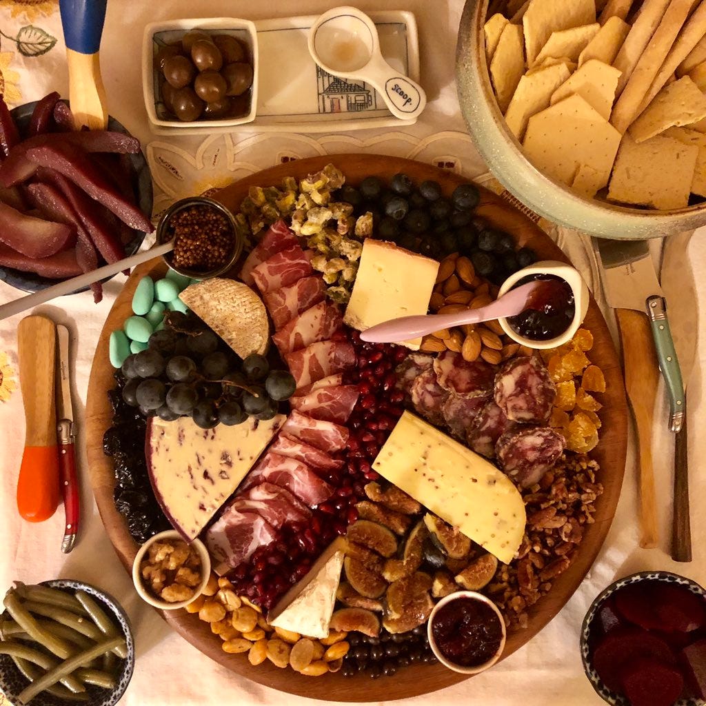 a large cheese plate with lots of small plates for fruit, pickles, crackers, and jams