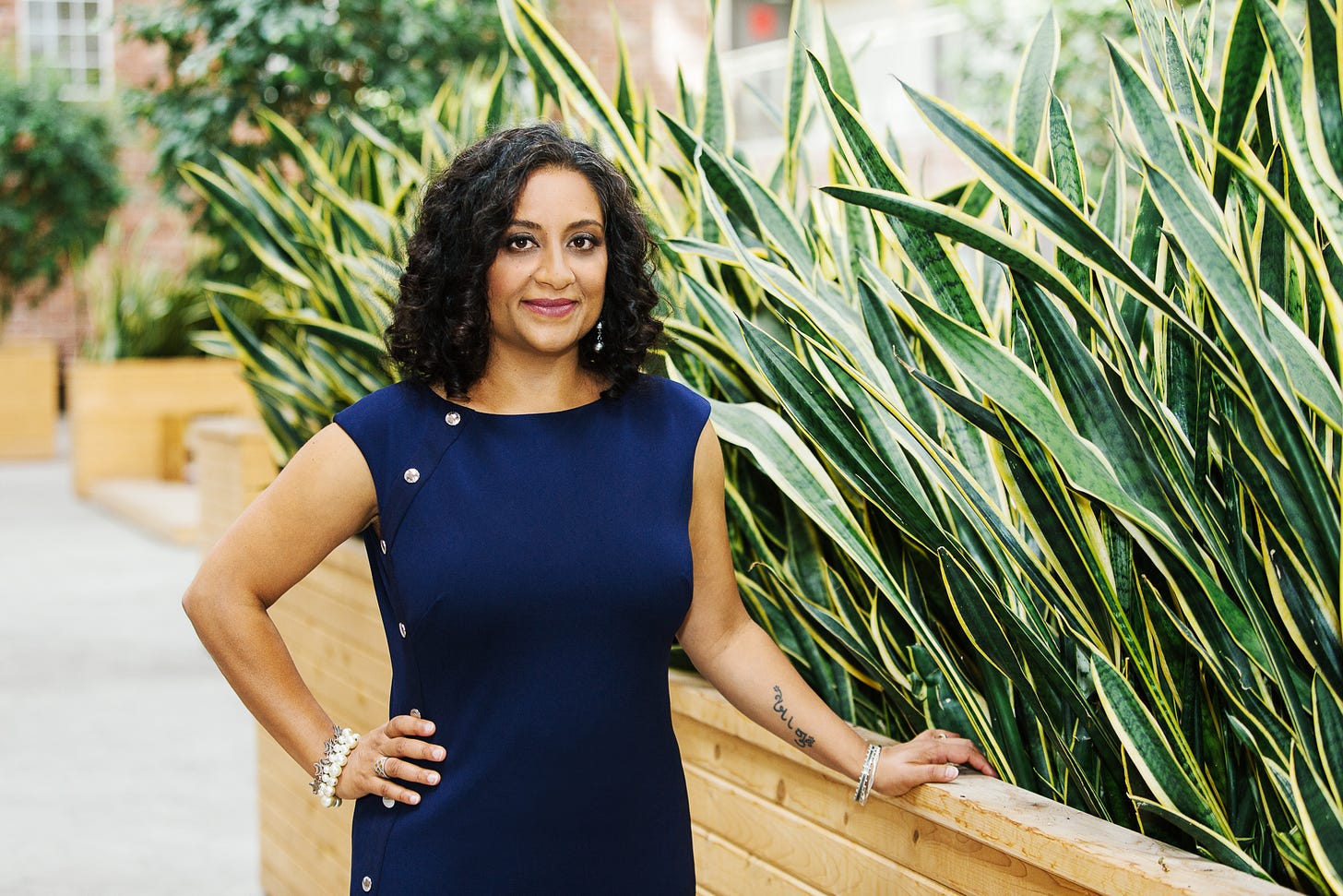 Farzana Doctor standing outside in a blue dress beside a large planter.