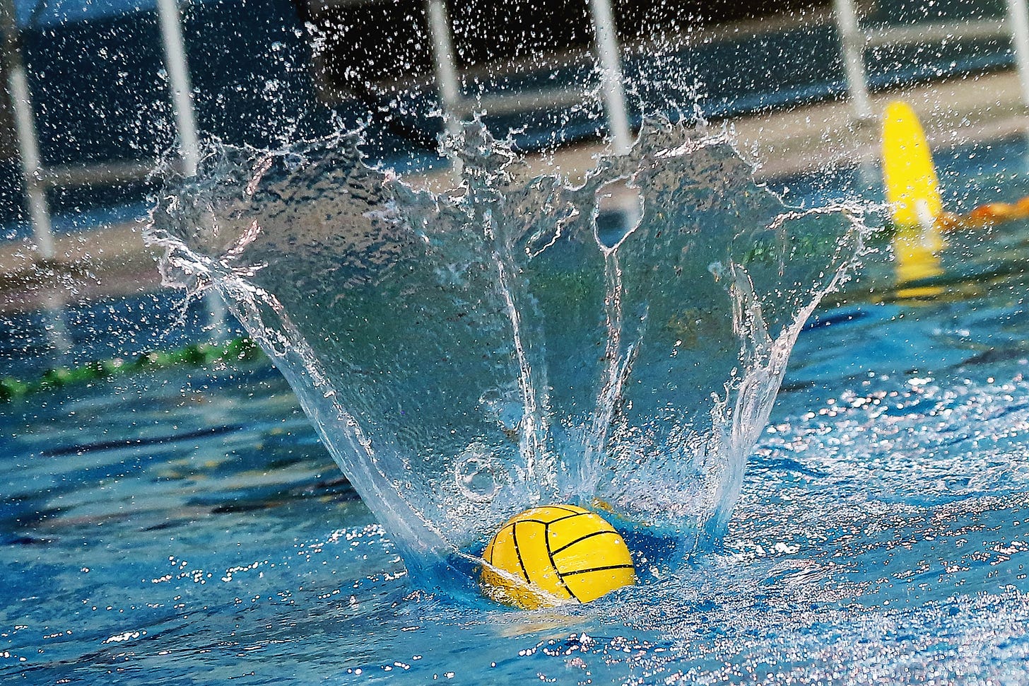 A water polo ball hitting pool water creating a huge conical splash