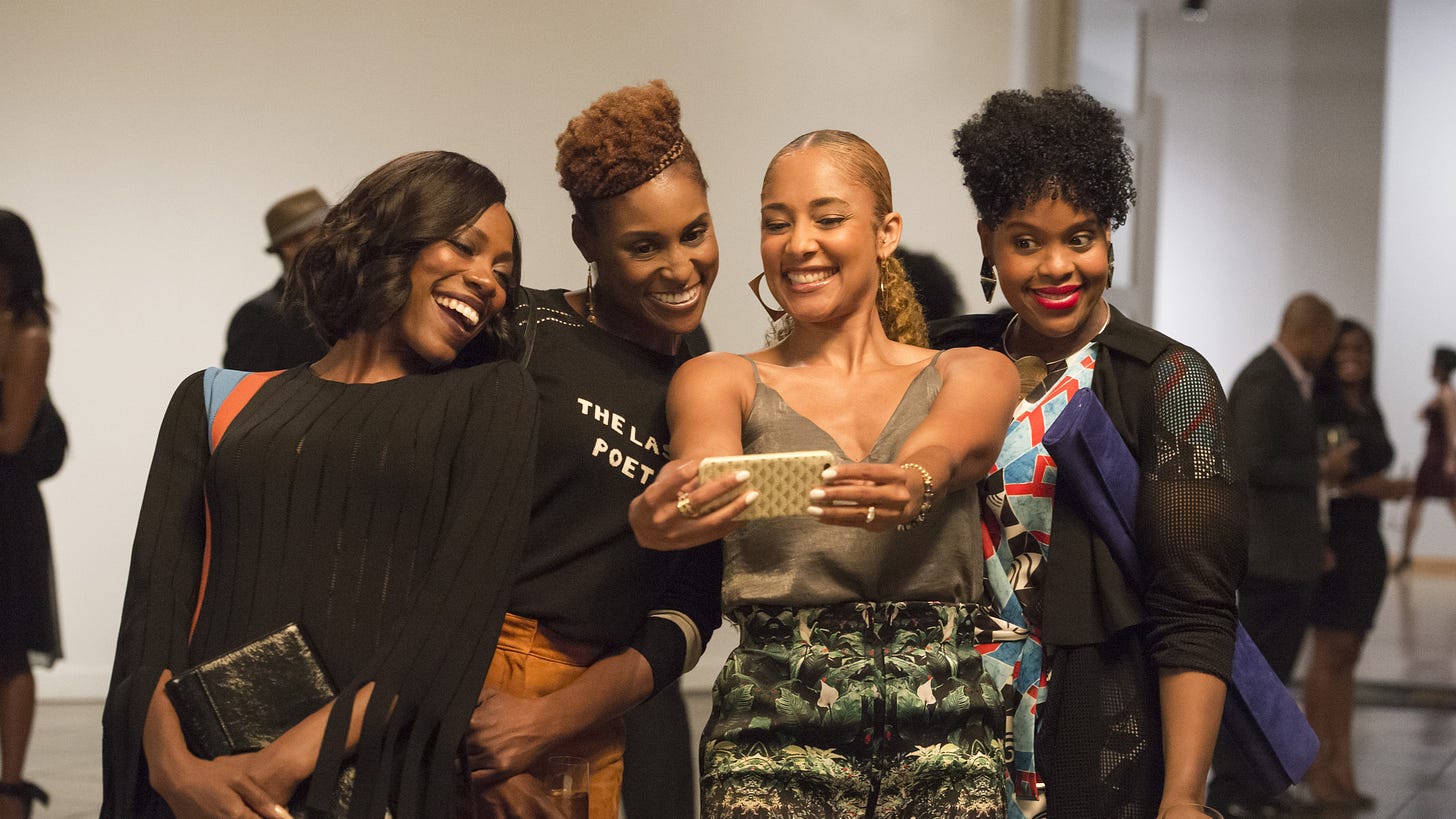 Four young Black women, in casua attire, pose for a selfie at an art gallery