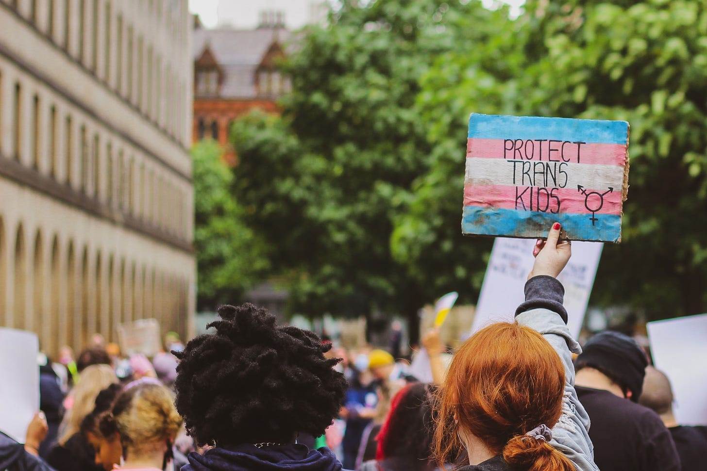 A sign at a protest is held up that says "Protect Trans Kids"