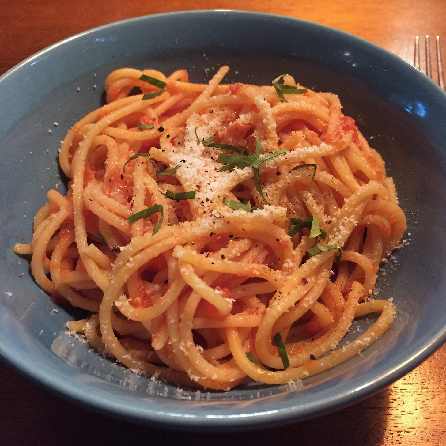 a blue bowl full of spaghetti in a light coating of tomato sauce, with a dusting of parmesan and shreds of basil.