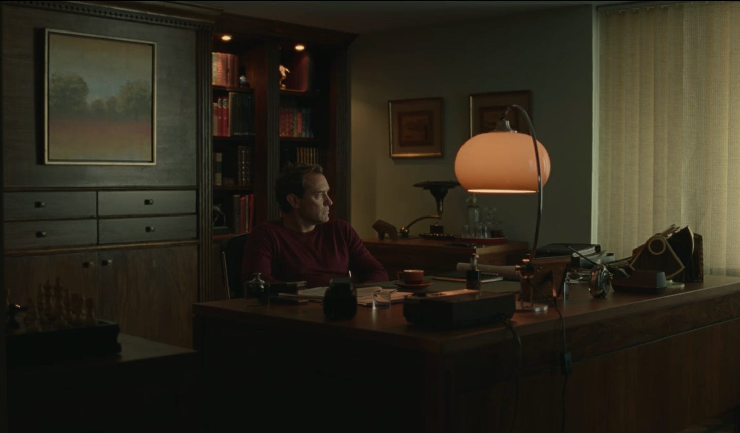 Jude Law in a home office, illuminated by a desk lamp, looking miserable, tbh