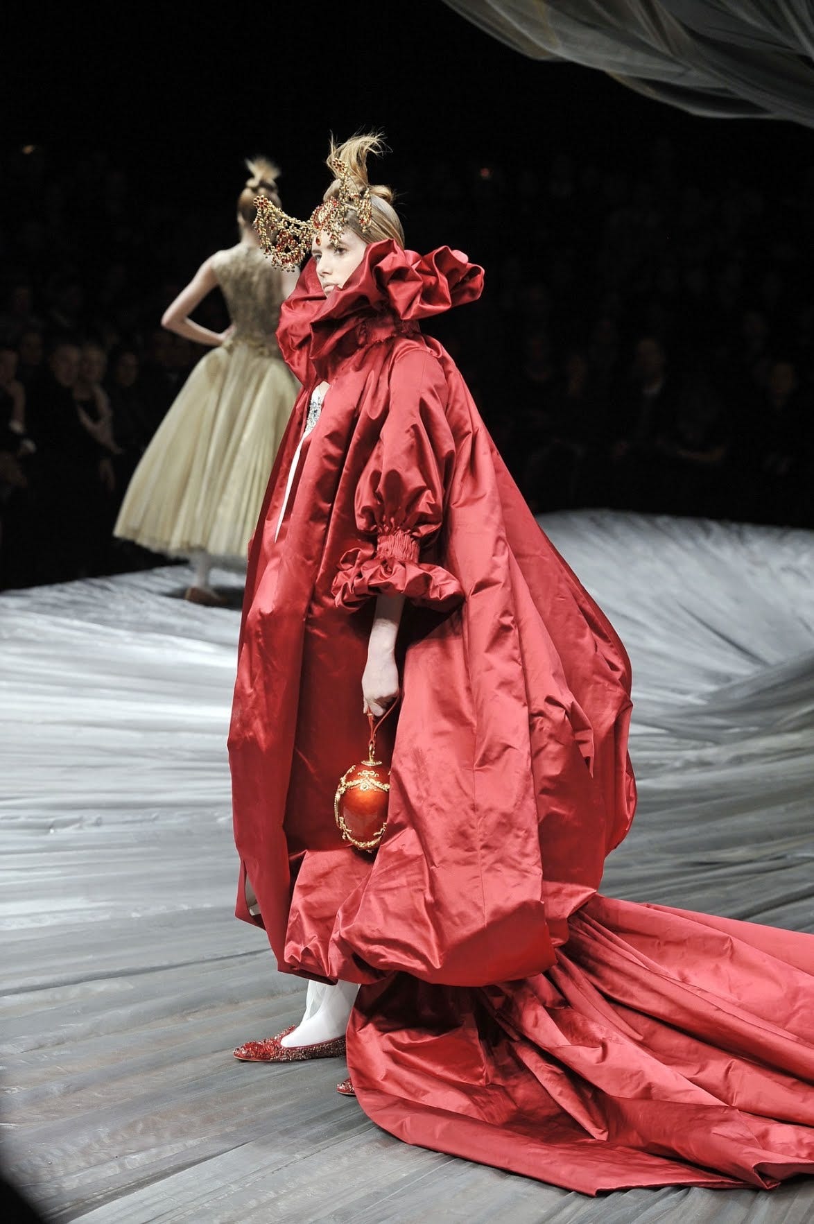 Una foto della sfilata della collezione autunno inverno 2008 di Alexander McQueen. Una modella indossa un elaborato cappotto rosso che ricorda un mantello