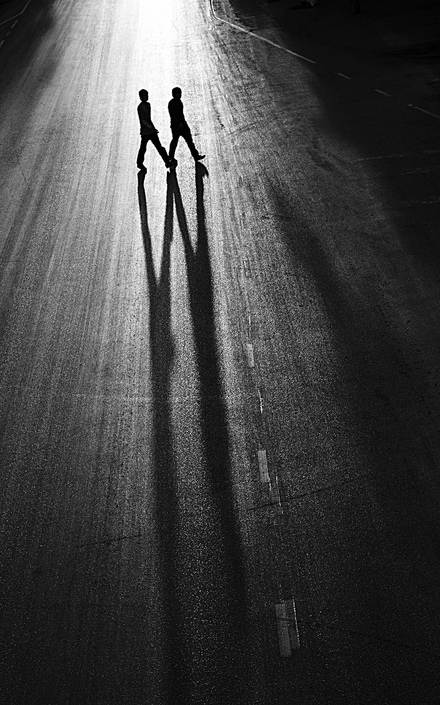 Long shadows cast by two  people crossing a street in the dark