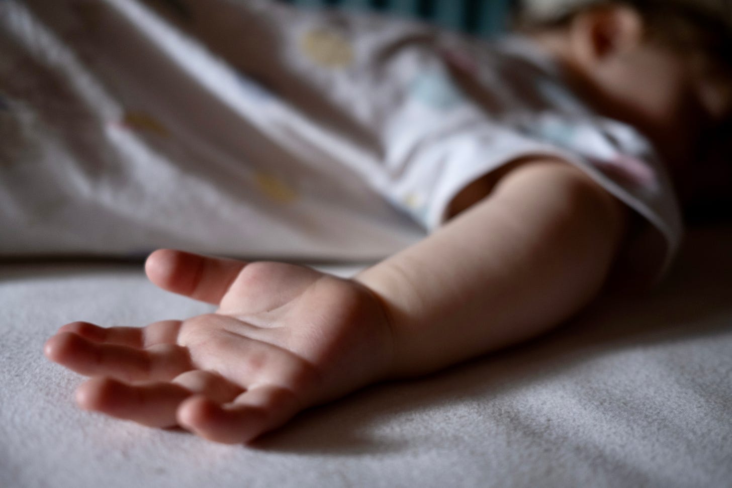 An out-of-focus child asleep, with a hand in the foreground.