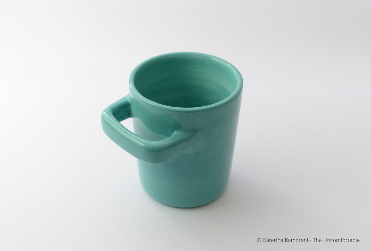 A tea mug with the handle misplaced so that it becomes impossible to drink from the cup.