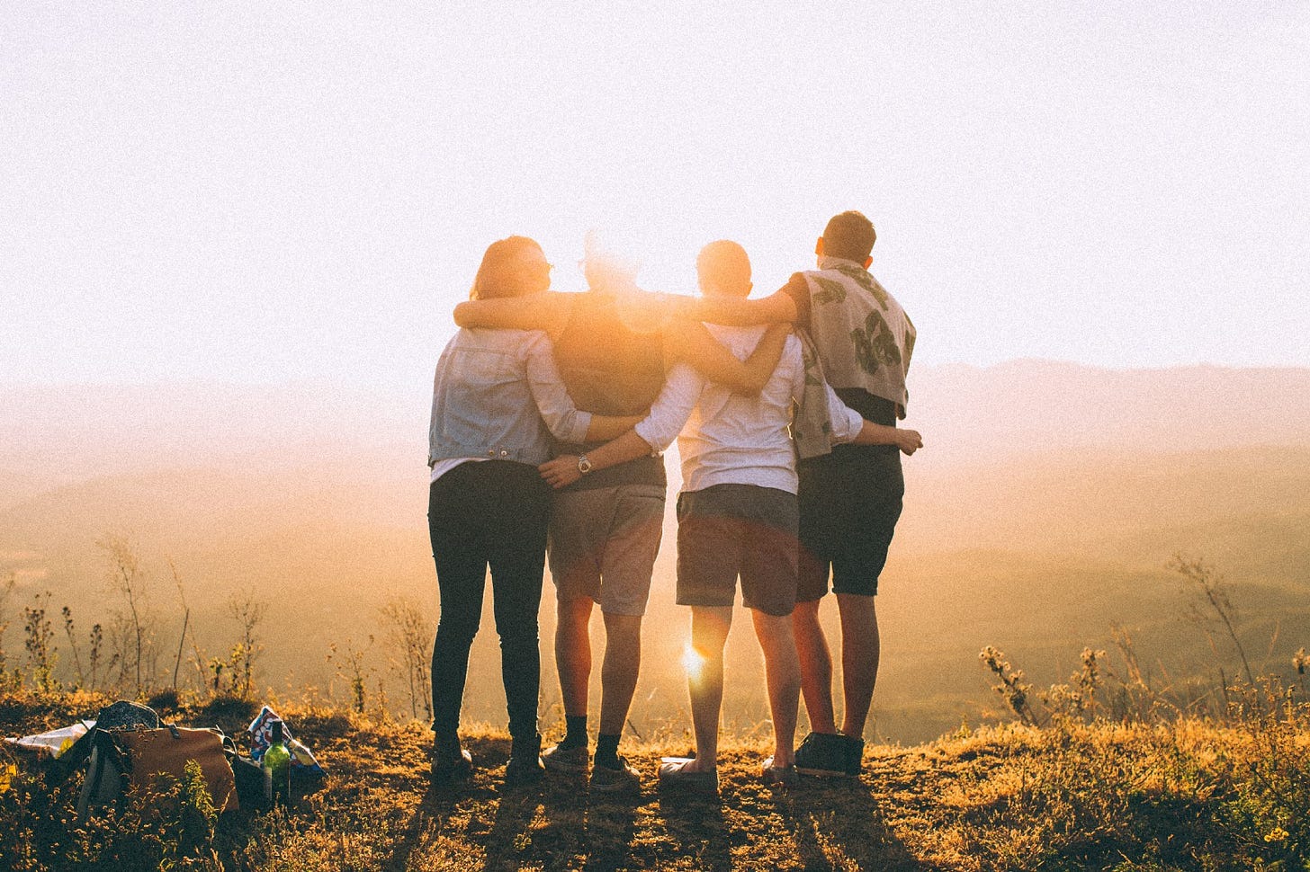 Four friends embrace on a mountaintop as the sun rises