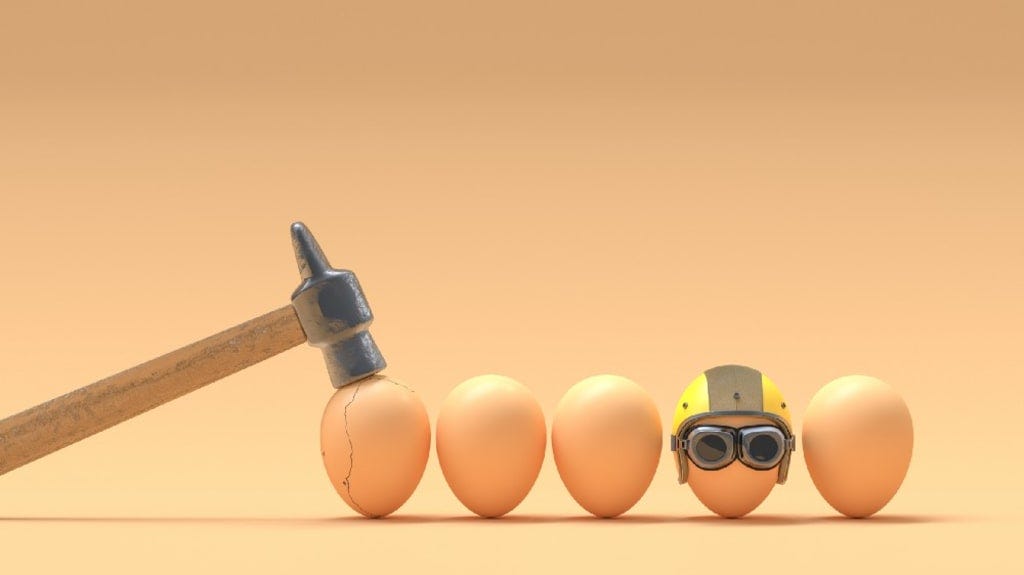 Image shows a hammer cracking an egg while another egg is safe, wearing a helmet
