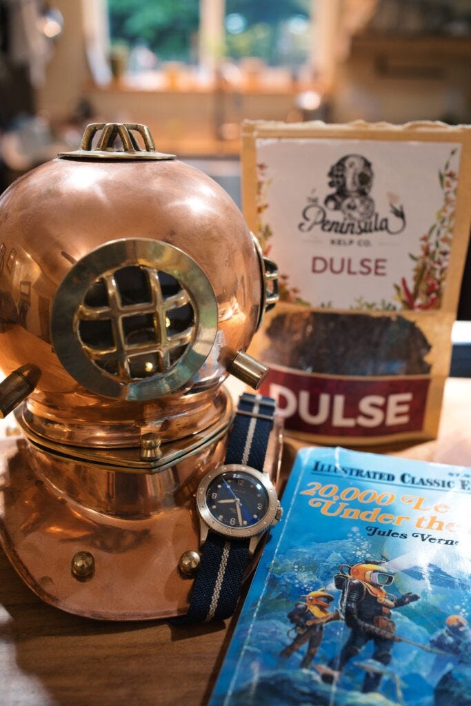 replica copper dive helmet with AJ's Baltic aquascaphe bronze laying on it (back when it was new before the pandemic) with a bag of dulse in background on a kitchen top
